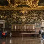 Tourists admire large ornate historical painting in museum.