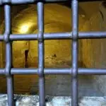 Old prison cell with barred window and stone walls.